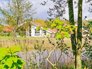 A house with a red roof, surrounded by trees and a body of water.