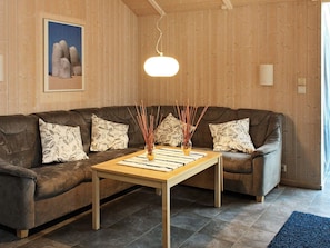 Um quarto com painéis de madeira, um sofá de couro marrom, almofadas estampadas, uma mesa de centro de madeira e um lustre.