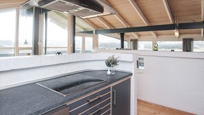 Una cucina moderna con una grande isola, forno integrato e vista sull'esterno grazie a ampie finestre.