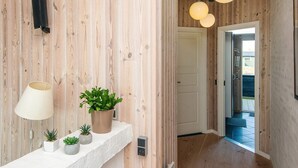 Un interno in legno con uno scaffale bianco con piante e una lampada, una porta che dà all'esterno e lampade a sospensione.