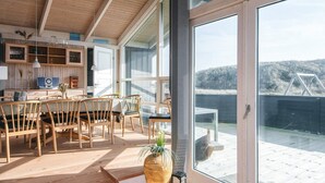 Un'ampia stanza con un'ampia porta-finestra scorrevole che dà su un patio esterno. All'interno, si trova un tavolo da pranzo in legno con sedie, un angolo cottura con pensili e un piano di lavoro, e un'ampia pianta in vaso.