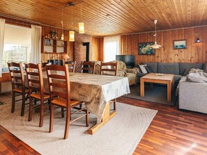 Un intérieur de chalet chaleureux avec une table à manger, des chaises, un canapé, un téléviseur et une cheminée.