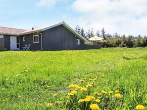 A house with a red roof, a front porch with two chairs, and a lawn with yellow flowers. - 10 Person Holiday Home in Lokken-by Traum (Lokken)
