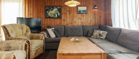 A cozy living room with a wooden ceiling, a large grey sofa, a wooden coffee table, and a television.