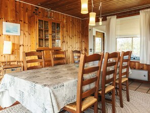A wooden interior with a dining table, chairs, a cabinet with glass doors, and a window with curtains.