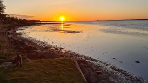 A sunset over a calm body of water with a grassy area and rocks in the foreground. - 5 Star Holiday Home in Storvorde (Storvorde)