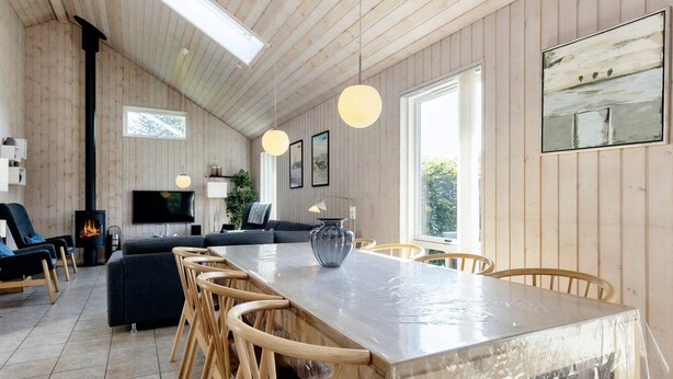 A modern kitchen with a long island, wooden chairs, and a large window. - 5 Star Holiday Home in Storvorde (Storvorde)