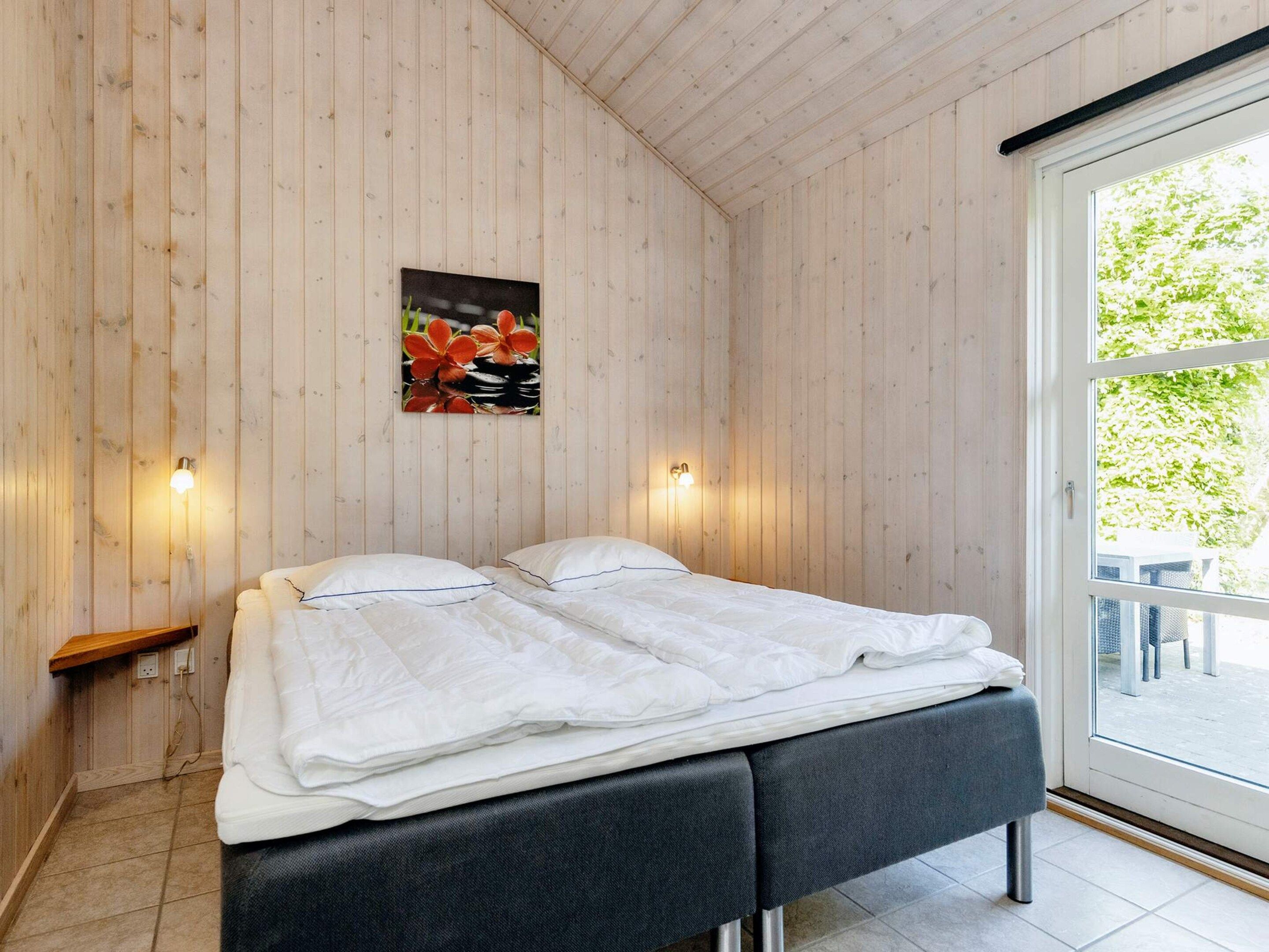 A room with a bed, two wall-mounted lights, a wooden wall, and a window.