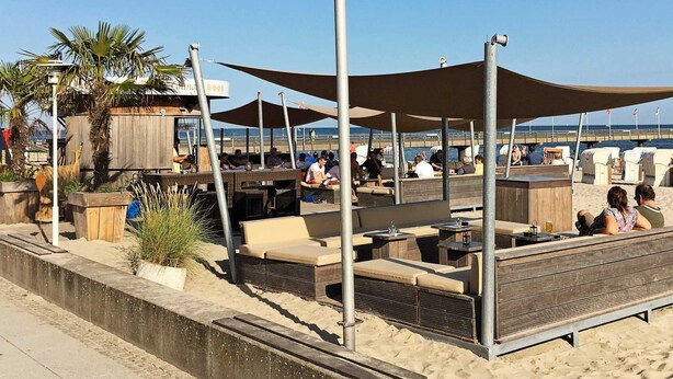 Un espace extérieur aménagé avec des tables et des chaises, une structure en bois et une vue sur la plage.