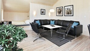 Un salon moderne avec un canapé d’angle, une table basse et une table à manger. Des tableaux encadrés ornent le mur et une plante en pot se trouve dans un coin.