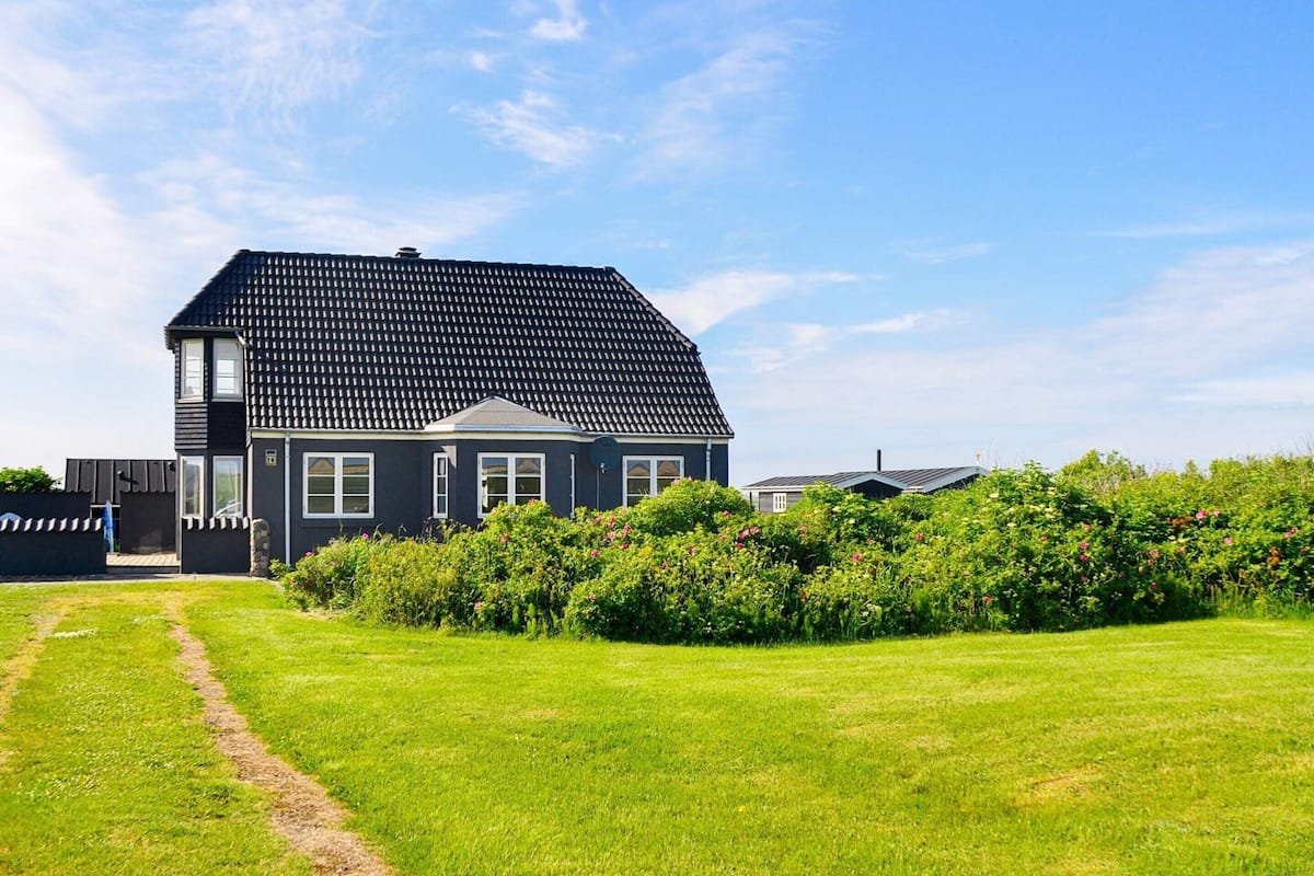 A two-story house with a dark roof and white trim, surrounded by a well-maintained lawn and dense shrubbery.