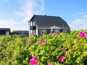 A two-story house with a dark roof and white trim, surrounded by lush greenery and pink flowers. - Tranquil Holiday Home in Lemvig near Sea (Lemvig)