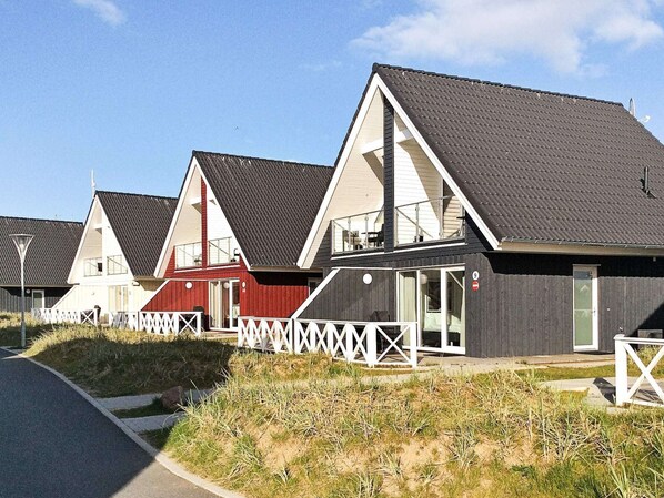 Una hilera de casas modernas frente a la playa, con techos inclinados, barandillas blancas y un cielo despejado.
