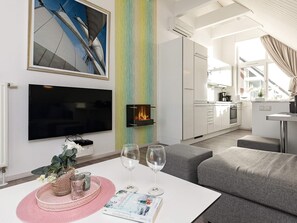 Un salon moderne doté d’un téléviseur à écran plat, d’une cheminée et d’un coin repas avec une table mise pour deux personnes.