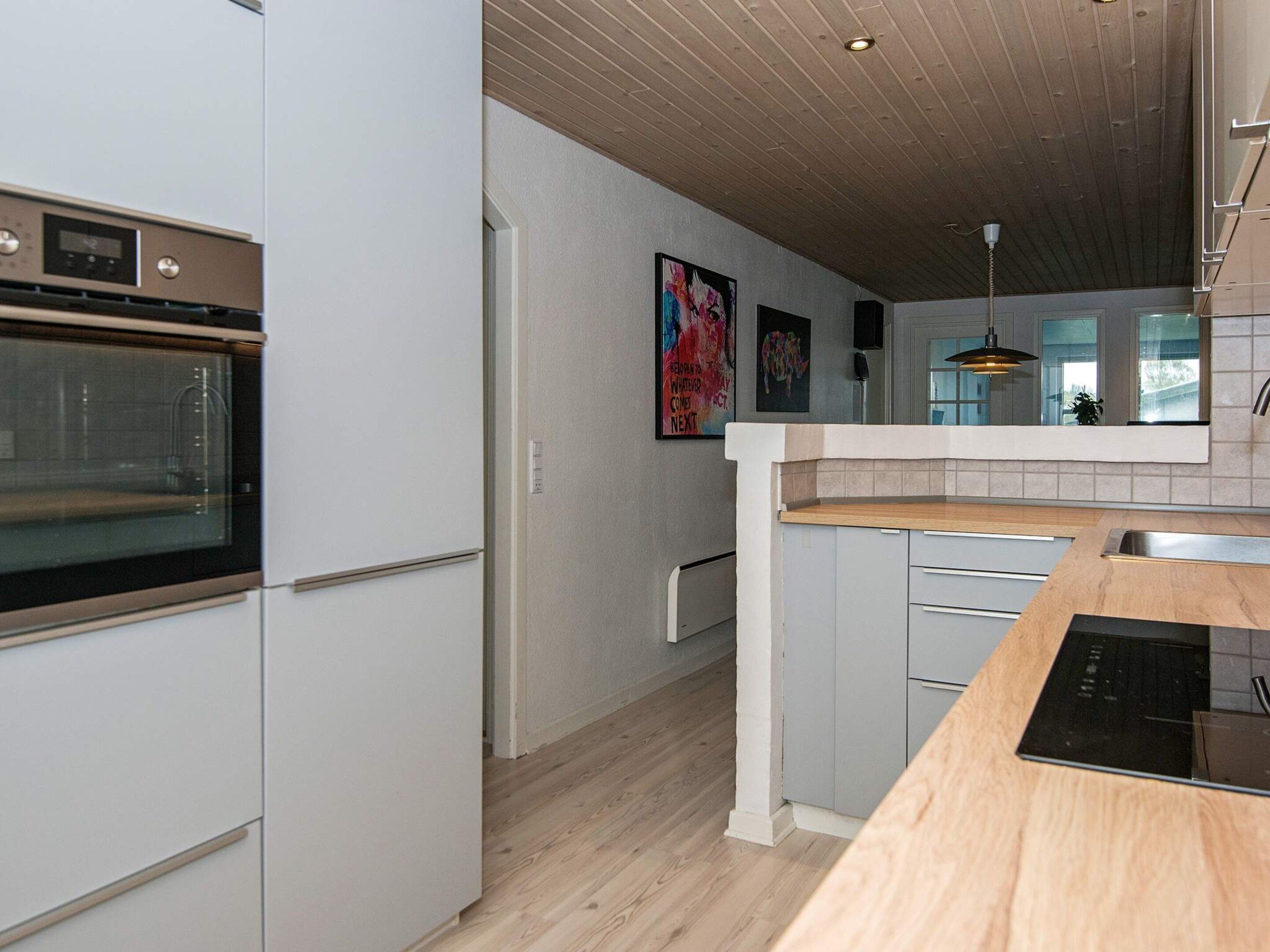 A modern kitchen with a built-in oven, wooden countertop, and a view into the adjacent living area.