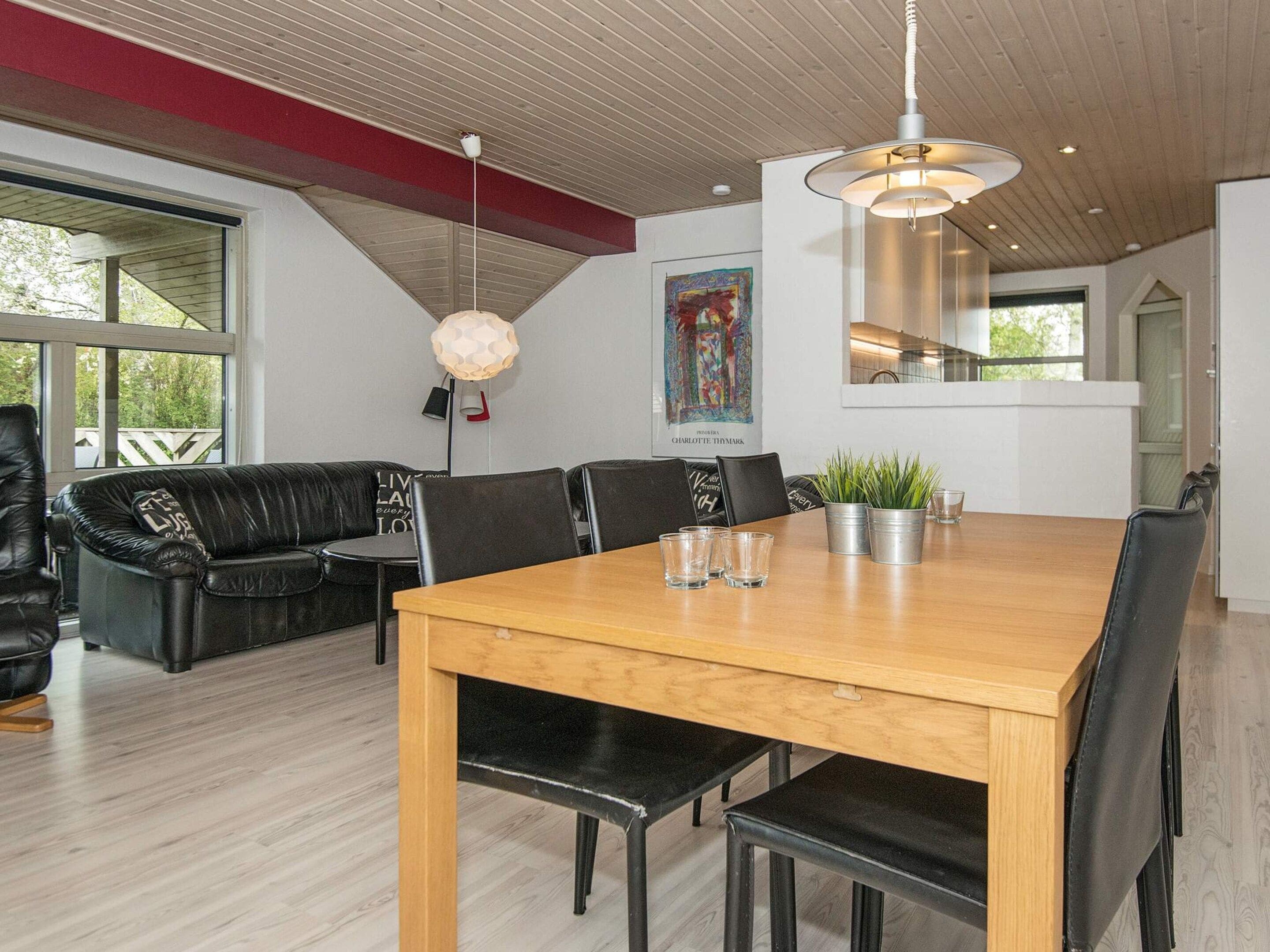 A modern dining area with a wooden table, black chairs, and a hanging light fixture.