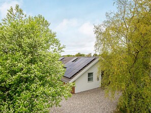 A house with solar panels on the roof, surrounded by trees and a gravel driveway. - 4 Star Holiday Home in Juelsminde (Horsens)