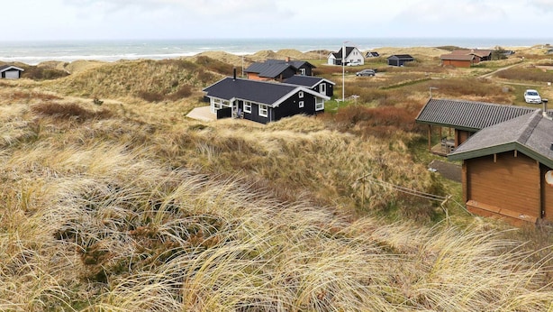Ett kustområde med hus omgivna av sanddyner och gräsmark.