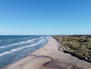 A coastal landscape with a sandy beach and grassy terrain. - 6 Person Holiday Home in Hirtshals (Hirtshals)