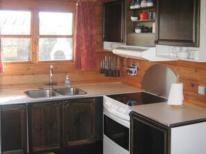 A compact kitchen with wooden cabinets, a sink, a stove, and a window with a curtain. - 6 Person Holiday Home in Hirtshals (Hirtshals)