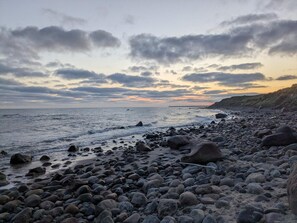 A rocky beach with waves, a ship in the distance, and a cloudy sky. - 6 Person Holiday Home in Hirtshals (Hirtshals)