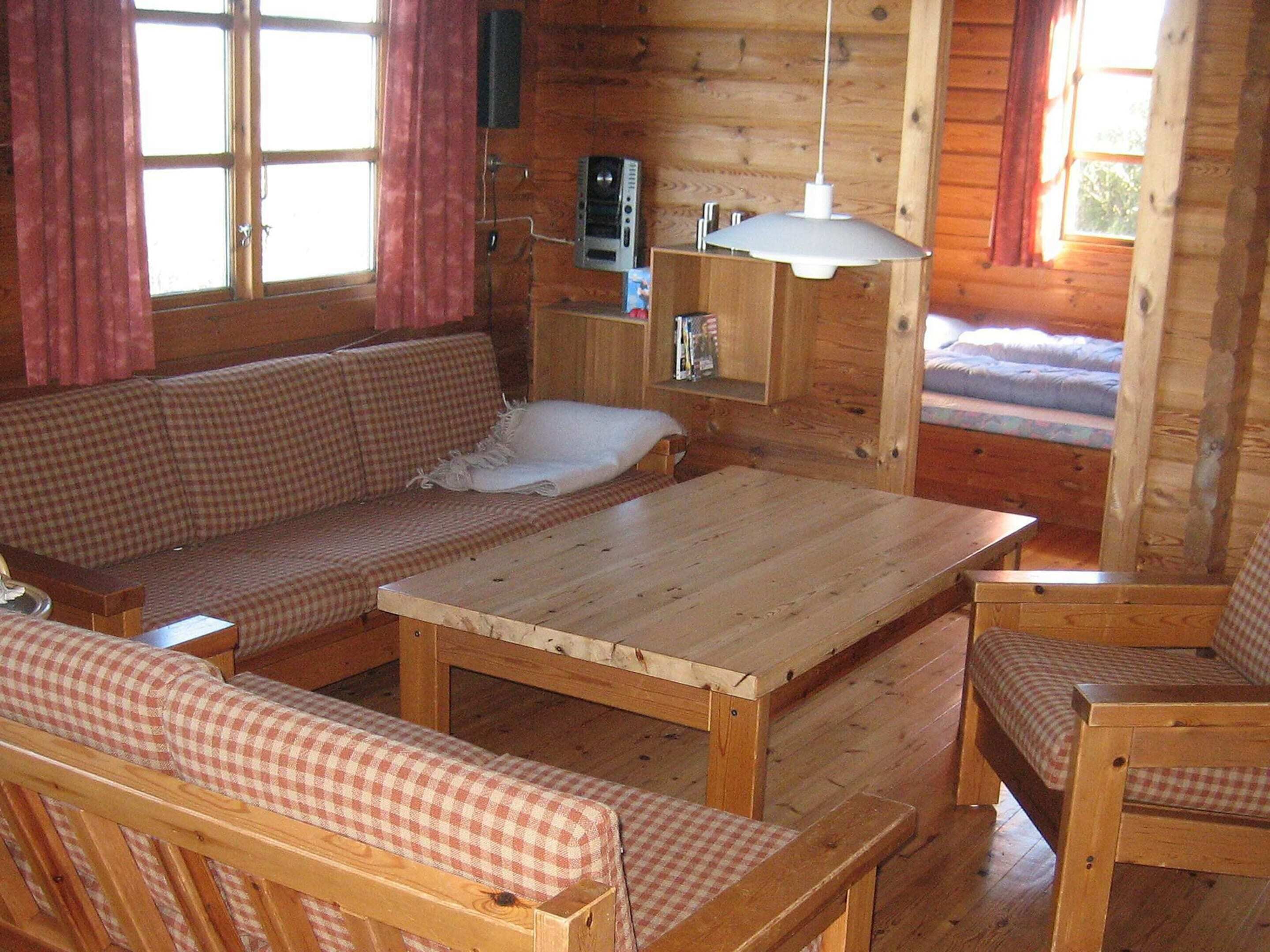A cozy cabin interior with a wooden floor, a checkered sofa, a wooden table, and a bench.