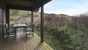 En träveranda med ett bord och stolar, med utsikt över ett grönskande landskap med få träd.