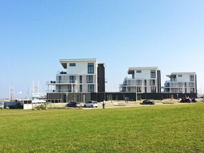 A modern building with multiple floors and balconies, situated near a grassy area with parked cars. - Holiday Home in Wendtorf (Wendtorf)