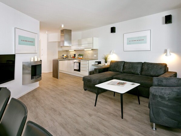A modern living room with a grey sofa, a coffee table, and a TV mounted on the wall. - Holiday Home in Wendtorf (Wendtorf)