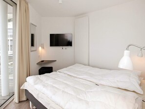 A hotel room with a bed, a television, a bedside table, and a window with curtains. - Holiday Home in Wendtorf (Wendtorf)