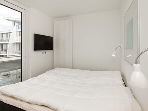 A modern bedroom with a large bed, a mounted TV, and a bedside lamp.