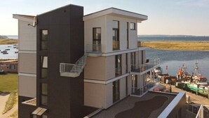 A modern multi-story building with a balcony, located near a body of water with boats. - Holiday Home in Wendtorf (Wendtorf)