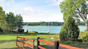 A lakeside view with a red fence, a sailboat, and a forested background.