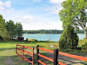 A lakeside view with a red fence, a sailboat, and a forested background. - Holiday Home in Väddö (Väddö)
