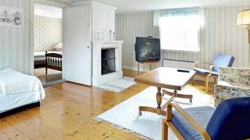 A room with a bed, a small table, a chair, a television, and a fireplace.