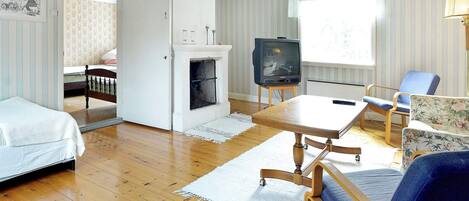 A room with a bed, a small table, a chair, a television, and a fireplace.