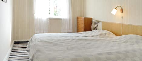 A hotel room with a bed, a dresser, a mirror, a window with curtains, and a wall-mounted light fixture.