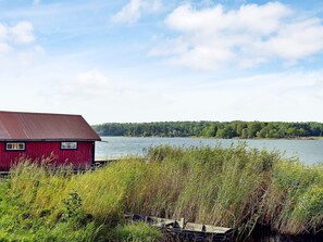 A red building with a metal roof near a body of water, surrounded by dense vegetation. - Holiday Home in Väddö (Väddö)