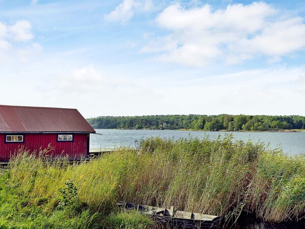 A red building with a metal roof near a body of water, surrounded by dense vegetation. - Holiday Home in Väddö (Väddö)