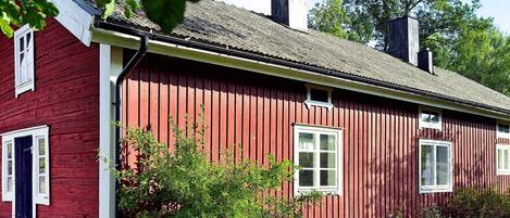 Une maison en bois peinte en rouge, avec des bordures blanches, des fondations en pierre et une cheminée.