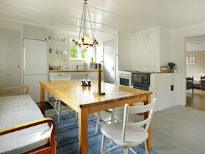 A kitchen with a wooden table, white chairs, a hanging light fixture, and a refrigerator. - Holiday Home in Väddö (Väddö)