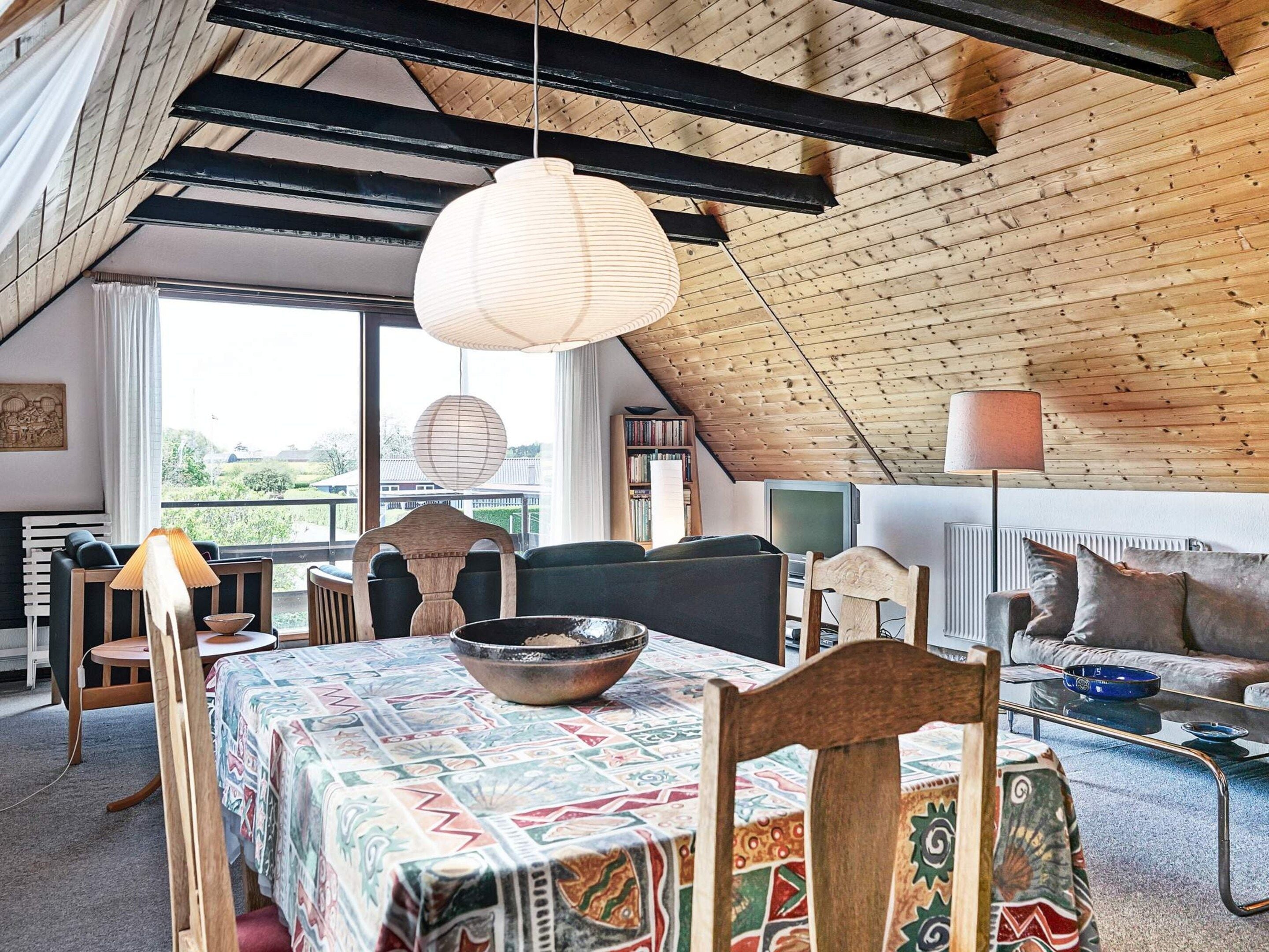 A cozy loft-style room with a sloped ceiling, a dining table with a patterned tablecloth, and a mix of modern and traditional furniture.
