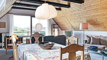 A cozy loft-style room with a sloped ceiling, a dining table with a patterned tablecloth, and a mix of modern and traditional furniture.