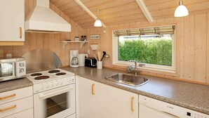 Ett modernt kök med träpanel på väggarna, en spis, en diskmaskin och ett fönster med utsikt över grönområden.