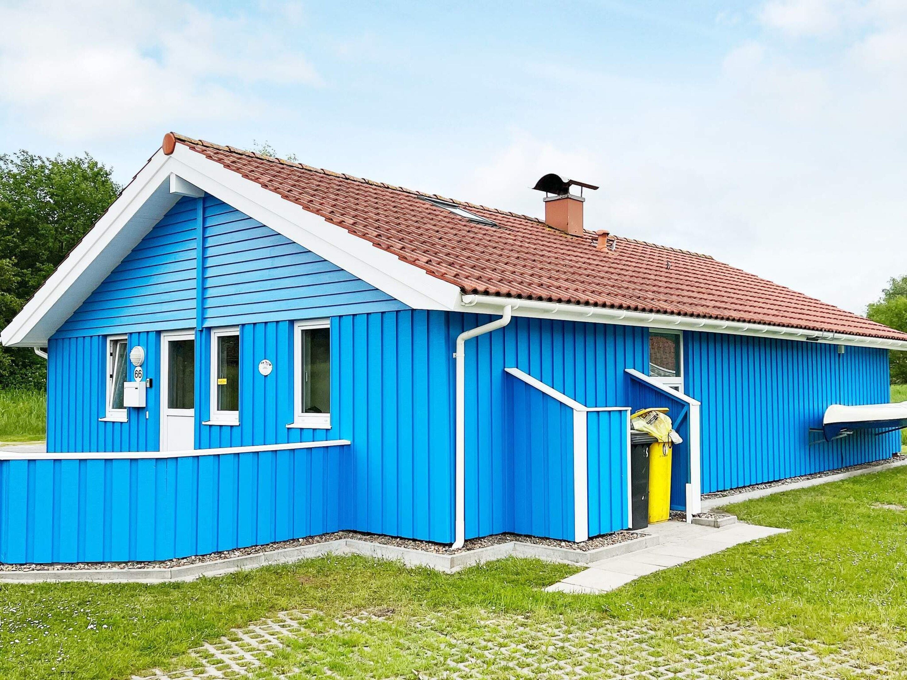 Un bâtiment bleu avec un toit recouvert de tuiles rouges, une cheminée et un petit porche.
