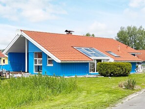 Ett blått hus med ett rött tak, en inglasad veranda och en liten trädgård.
