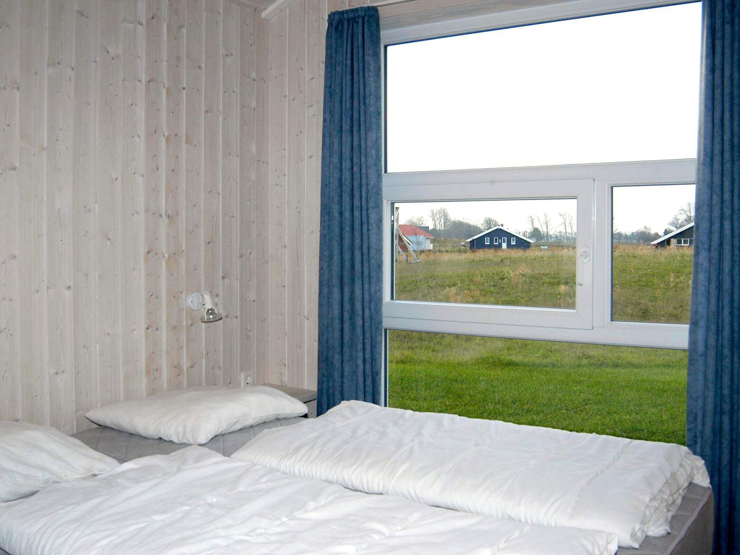 A bedroom with a large window, a bed with white bedding, and a wooden wall.