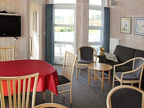 A room with a television, a red table, and a sofa with a cushion. - Holiday Home in Otterndorf (Otterndorf)