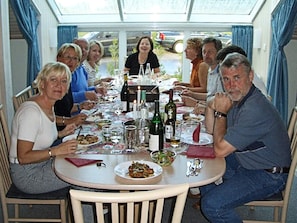 A group of people seated around a round table with food and drinks, in a room with a glass ceiling and curtains. - Holiday Home in Otterndorf (Otterndorf)