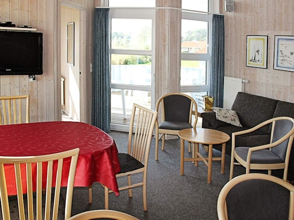 A room with a television, a red table, and a sofa with a cushion.